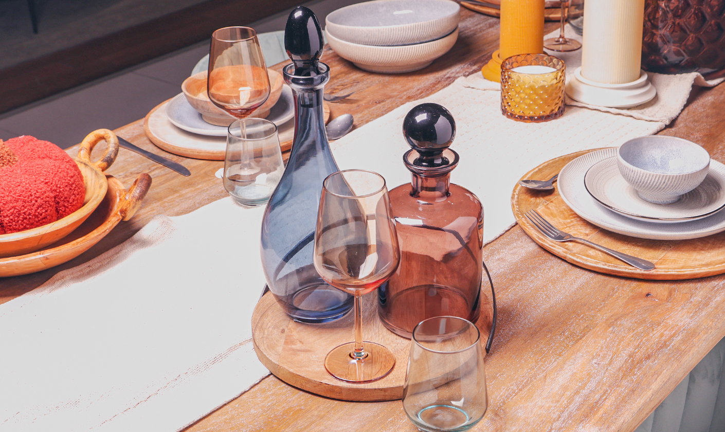 Minimal glassware arranged on a wooden dining table with decorative bottles.